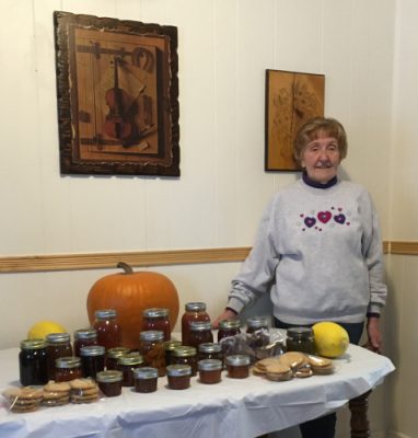Carole Blakeman beside a table of homemade jams and jellies, a pumpkin and homemade cookies